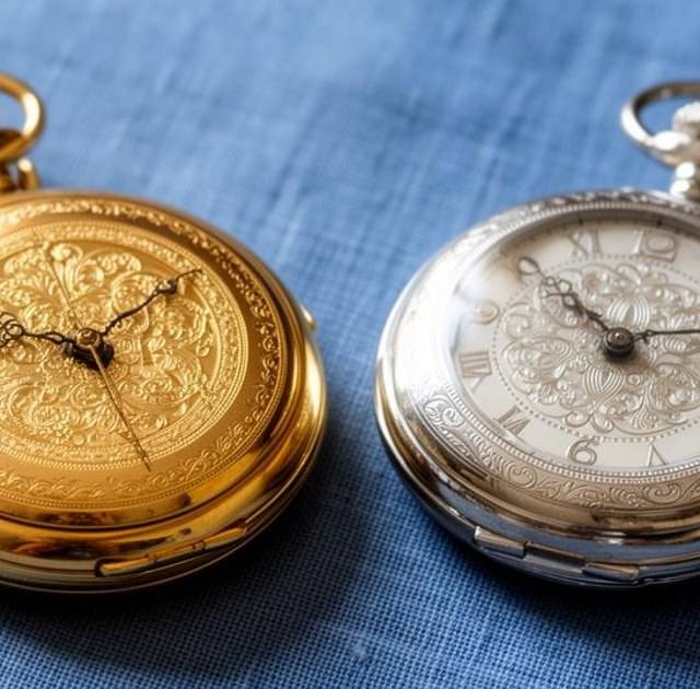 An antique gold pocket watch beside a silver pocket watch on blue linen
